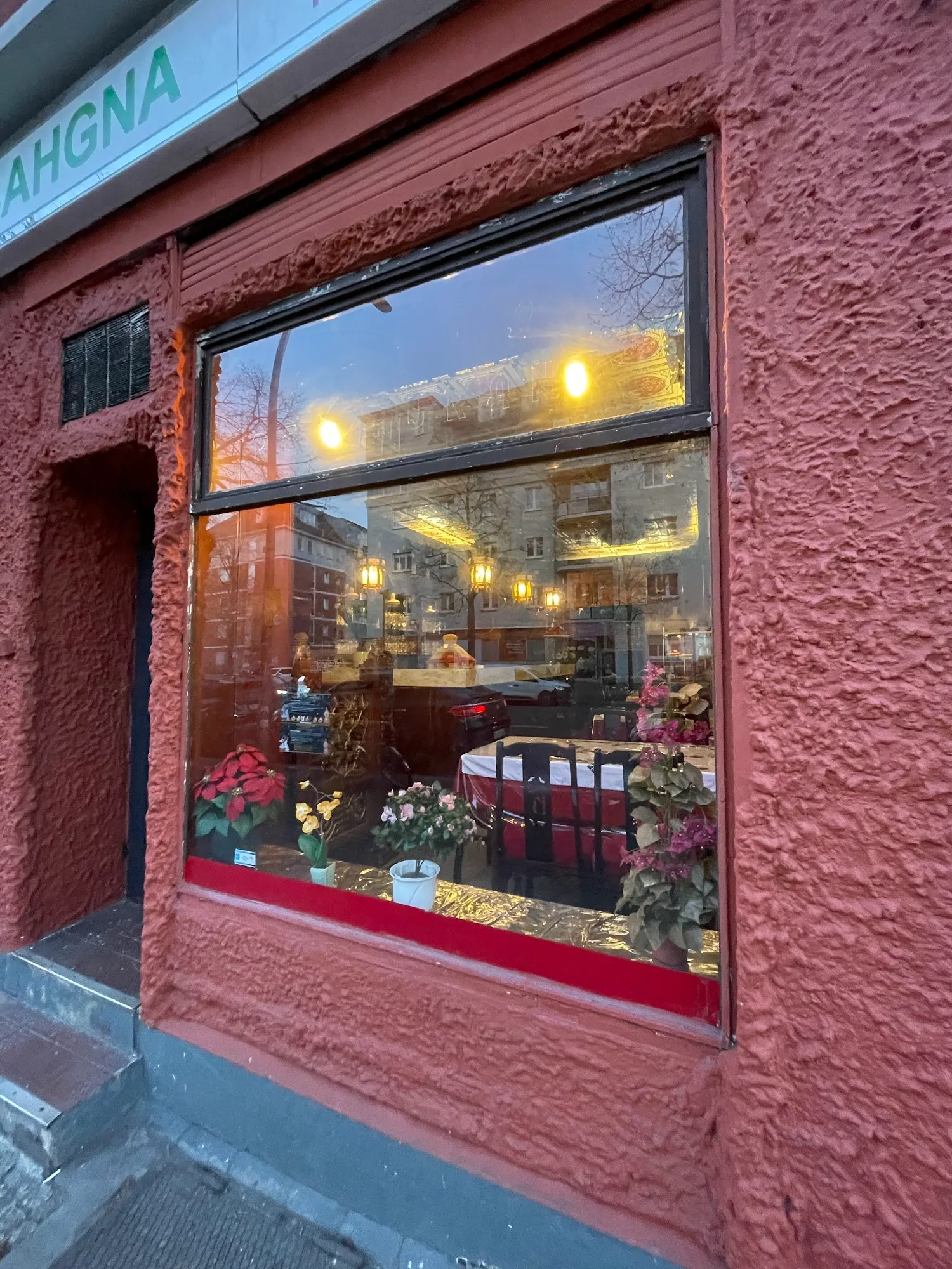 Fensterfront von Bahgna mit roter, strukturierter Fassade, Pflanzen und warmem Licht dahinter