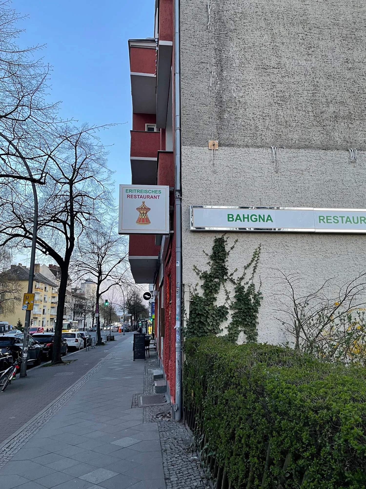 Blick den Bürgersteig am Britzer Damm entlang auf das auskragende Schild von Bahgna