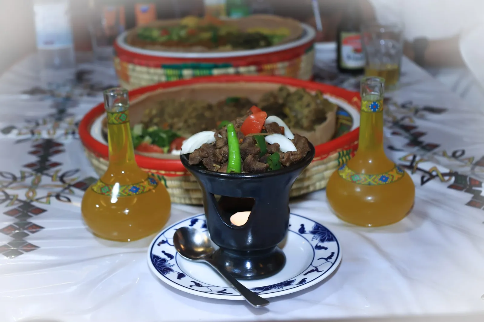Tibsi: gebratene Rindfleischwürfel mit grünen Bohnen, Tomate und Zwiebel, serviert im schwarzen Tontopf über einem Teelicht-Wärmer, daneben Karaffen mit Tej